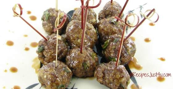 Saucy Asian meatballs with toothpicks in them on a white plate with dots of sauce surrounding them.