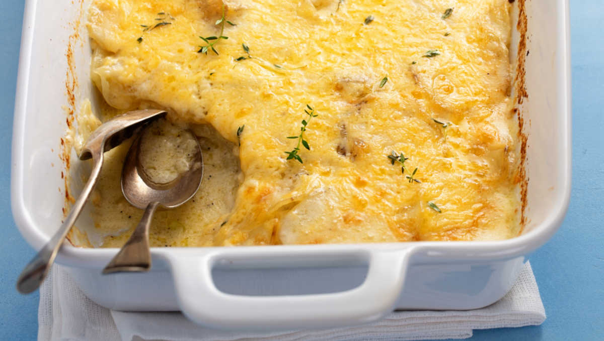 Cheesy scalloped potatoes in a white baking dish with two spoons.