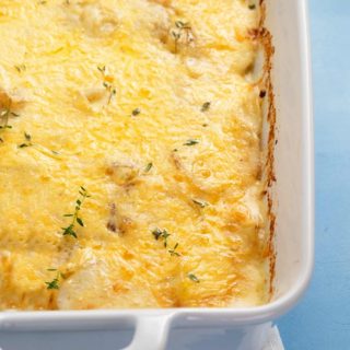 Scalloped potatoes au gratin in a white casserole dish on a blue background.
