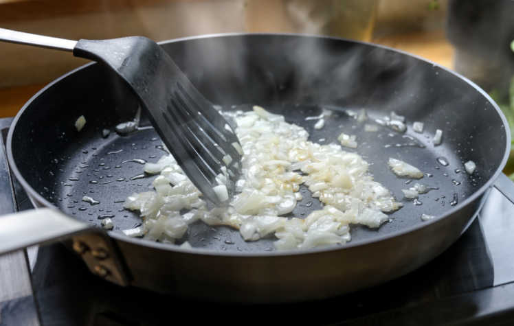 Cook the onions A spatula stirring cooked onions in a frying pan.