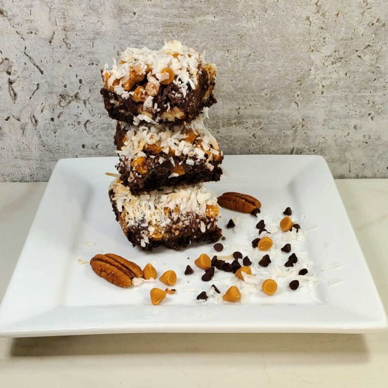 A stack of Hello Dolly bars in a white plate with pecans, coconut, chocolate chips and butterscotch chips.