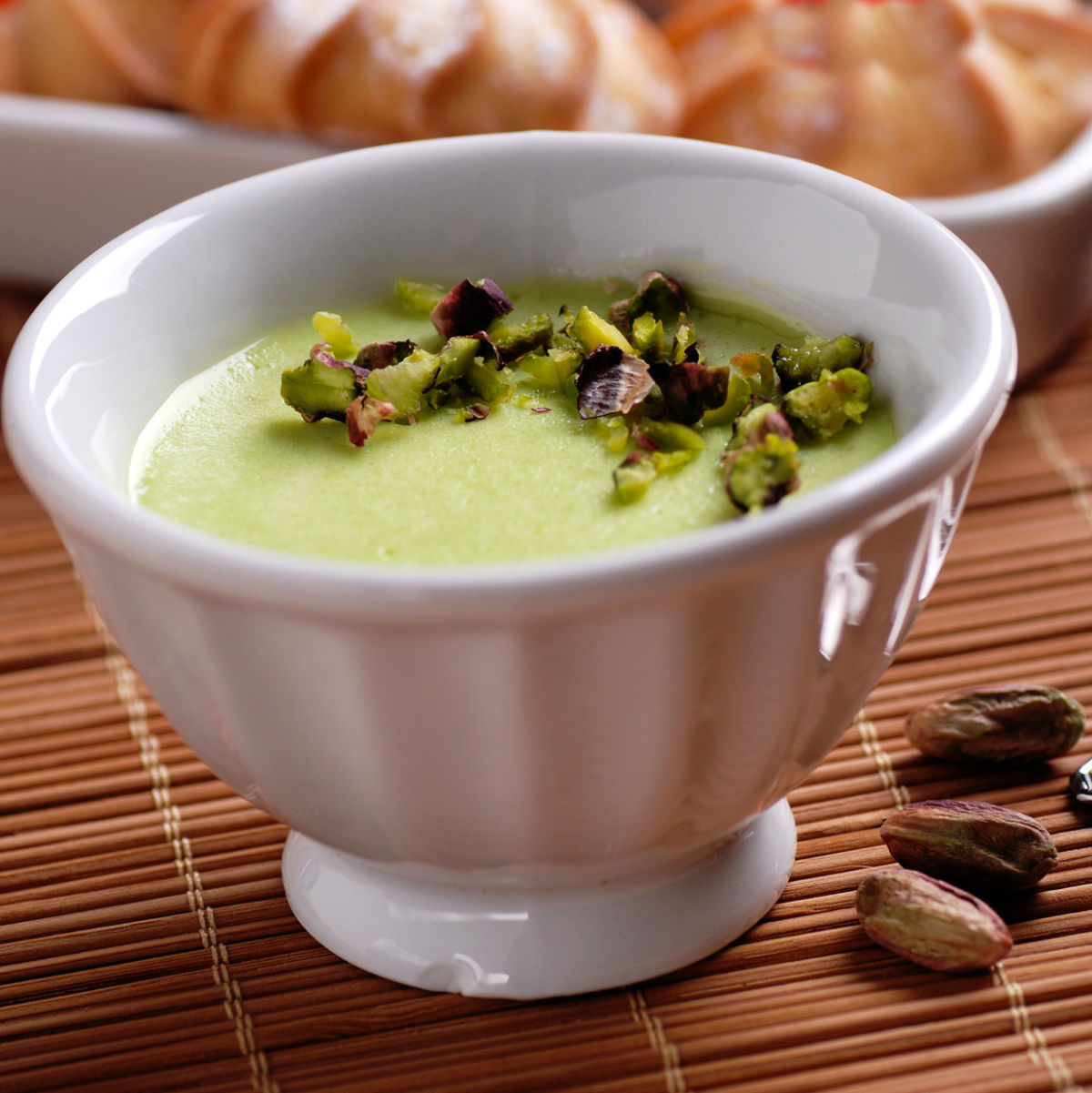 Homemade pistachio pudding in a white bowl on a bamboo mat.