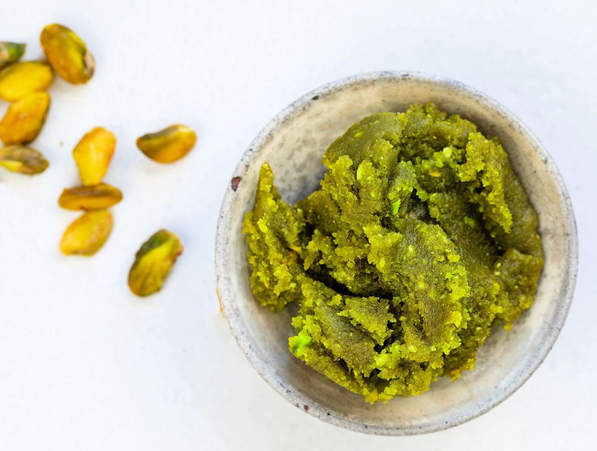 Bowl of pistachio paste next to some whole pistachios.