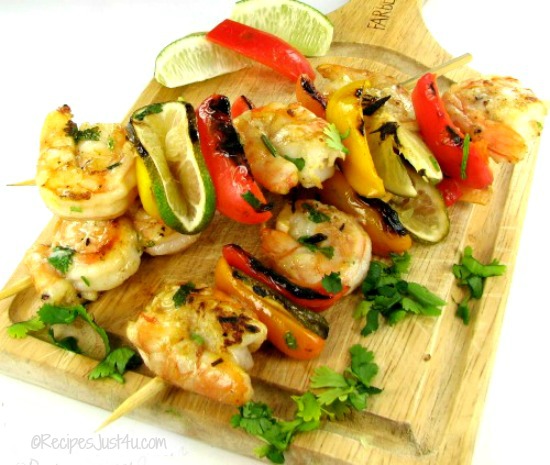 grilled cilantro lime shrimp kebabs on a wooden cutting board with limes.