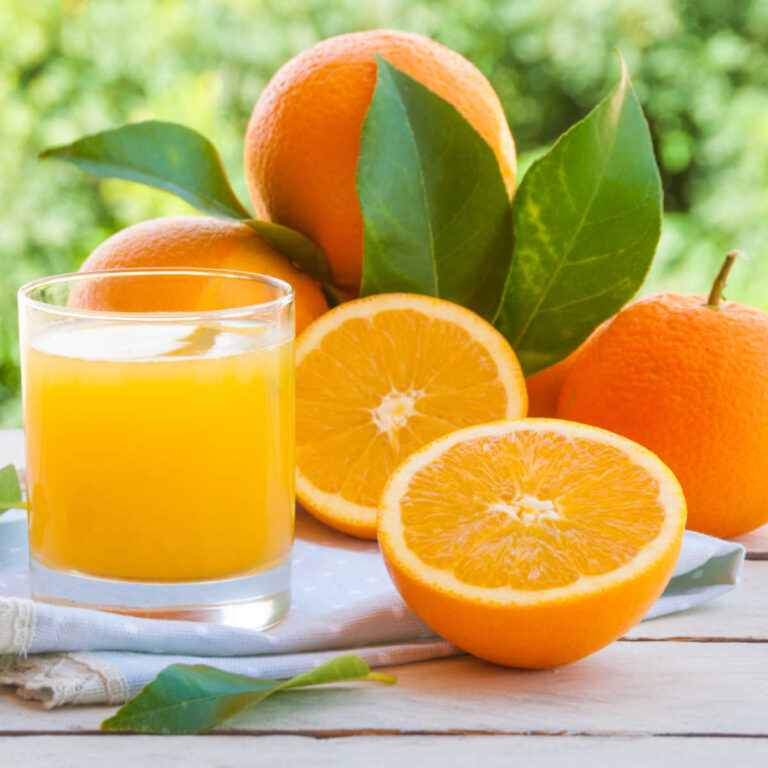 Glass of orange juice and cut fresh oranges on a wooden counter.