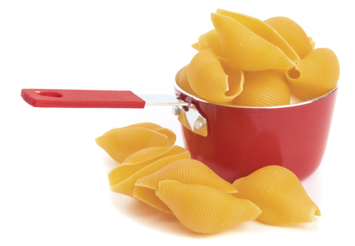Uncooked jumbo pasta shells in a red pot.