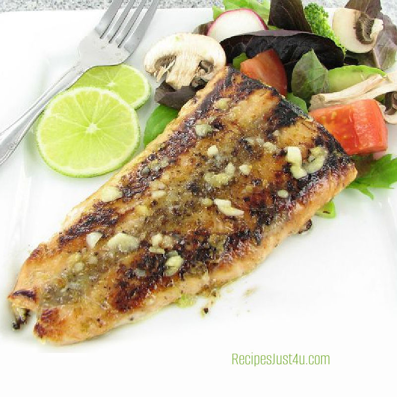 Honey garlic salmon on a white plate with lime and salad.