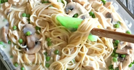 Creamy chicken tetrazzini A glass pyrex dish filled with a creamy chicken tetrazzini recipe, being stirred by a spatula with a wooden handle and green silicone tip.