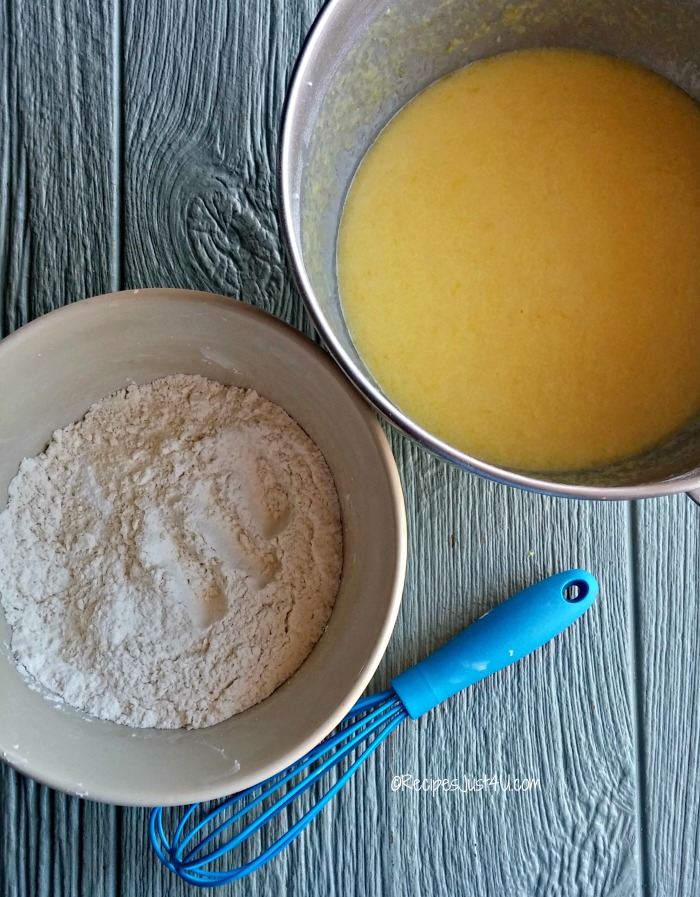 Wet and dry ingredients for lemon bundt cake in two bowls with a blue whisk.