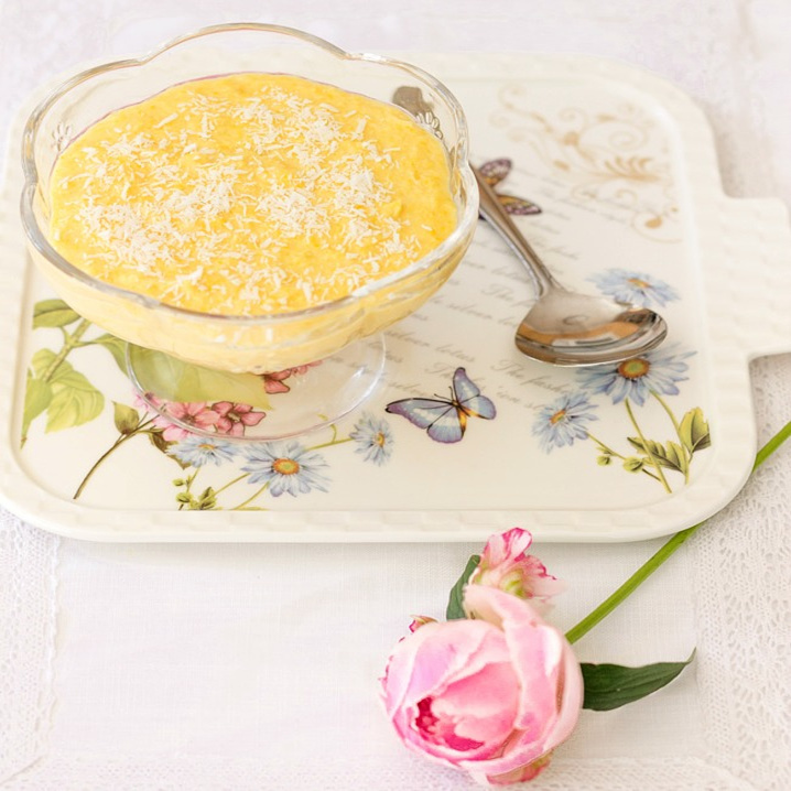 Coconut corn pudding in a glass bowl with a spoon on a flowered plate.