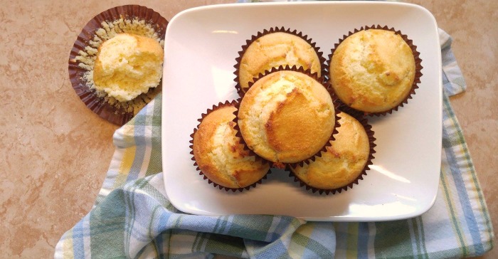Five buttermilk cornbread muffins sitting on a white plate, with a green and blue plaid cloth napkin beside it.