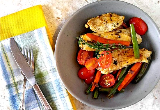 Balsamic chicken with vegetable in a gray bowl next to napkins and knife and fork.