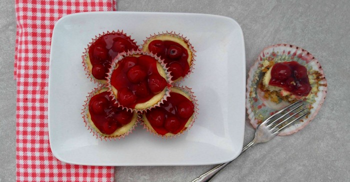 Mini cherry cheesecake cupcakes Five mini cherry cheesecake cupcakes on a white plate with a red gingham napkin.