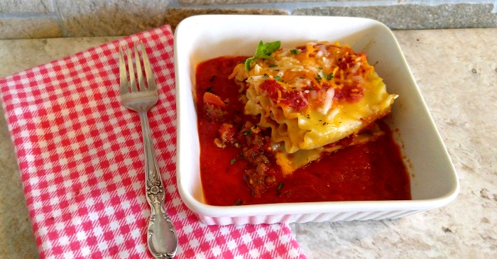 Lasagna roll ups in a white bowl with a red checked napkin and fork.