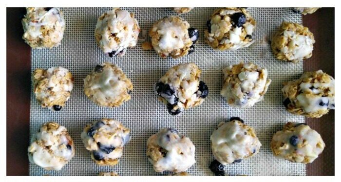 An overhead shot of blueberry energy balls with icing on a silicone baking mat.