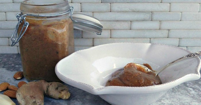 Almond butter salad dressing with a spoon in a white bowl next to a jar of the homemade dressing.