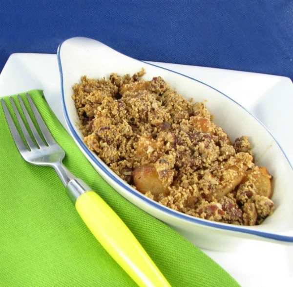 Apple and pear crisp in a white dish with a yellow spoon and green fork.