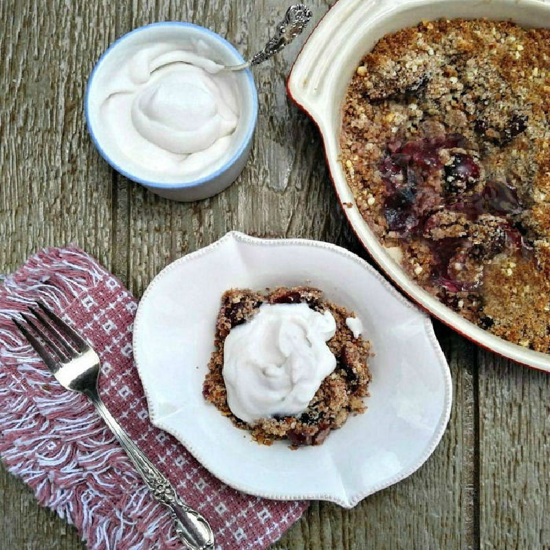 A gluten free cherry crumble recipe in a baking dish and serving dish with whipped coconut cream.