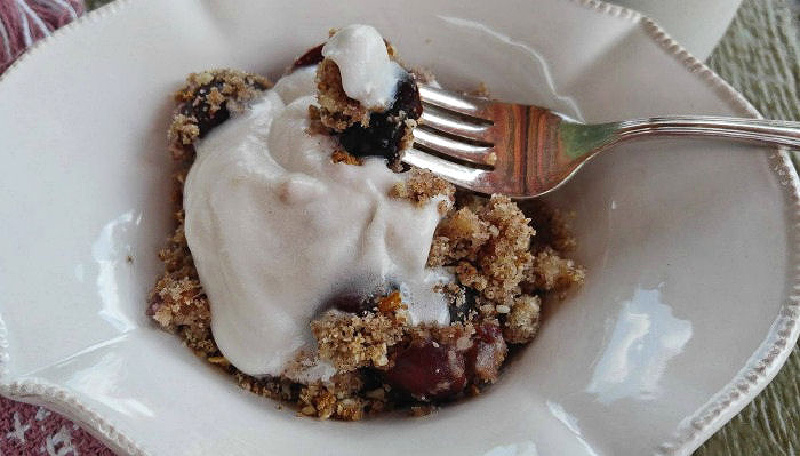 Healthy cherry crumble in a white bowl with whipped coconut cream.