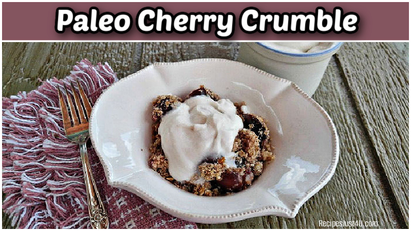 A serving of paleo cherry crumble recipe in a white bowl with homemade whipped coconut cream.