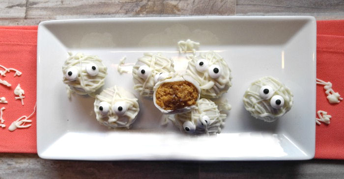 Pumpkin truffles decorated like mummies on a white plate.
