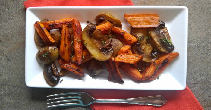 Roasted carrots and mushrooms with thyme on a white plate, with a red napkin under it, and a fork at the bottom of the plate.