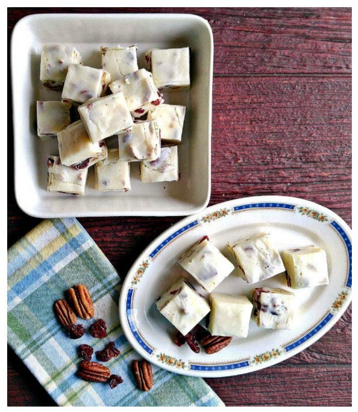 Cranberry pecan fudge in a bowl and on a plate with nuts and cranberries on a blue plaid napkin.