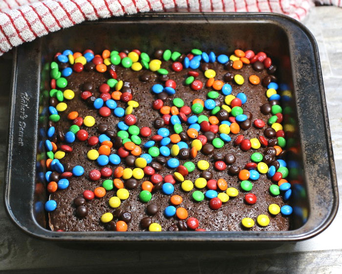 Adding M & M baking bits to the top of partially cooked brownies.