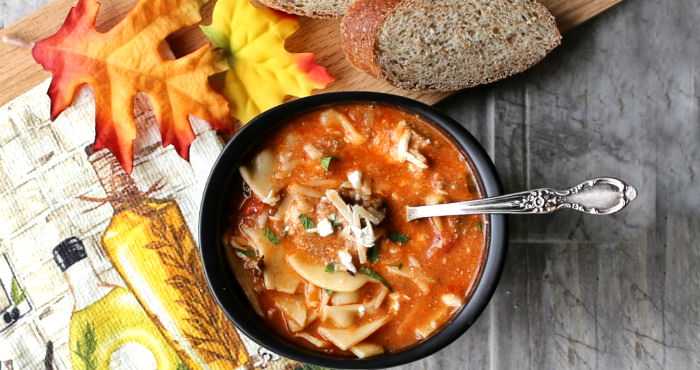 Lasagna soup in a black bowl, with a tea towel, fall leaves and bread surrounding it.
