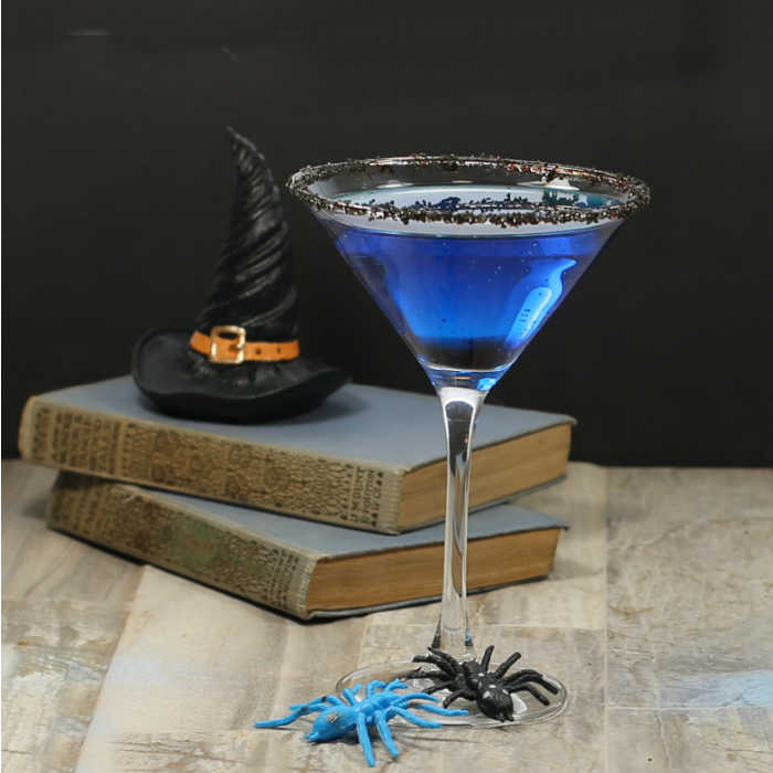 Blue drink in a martini glass with books and witches hat.
