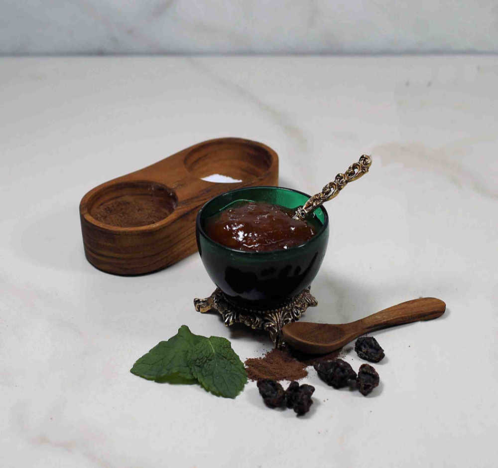 Chutney in a green jar with a gold spoon with mint, spices and raisins.