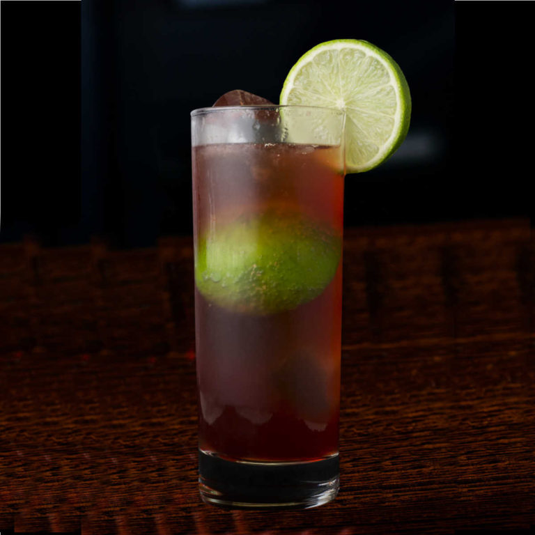 El Diablo Drink, consisting of tequila, creme de cassis, ginger ale and lime juice. Isolated on a wooden table with a black background.