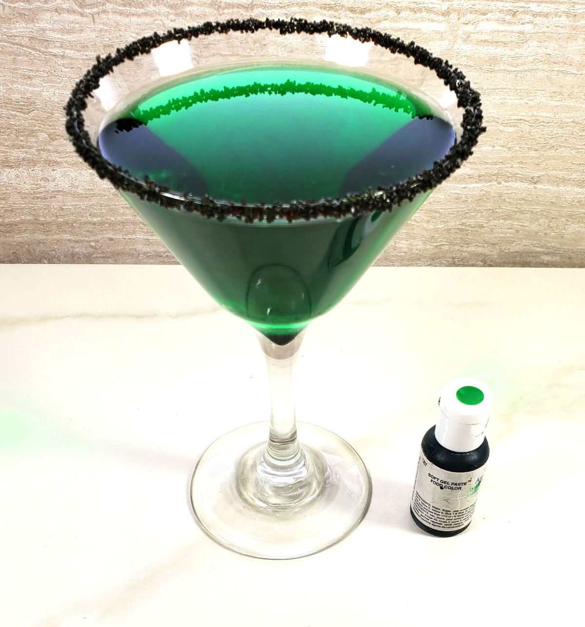 Green food coloring next to a green martini drink with a black rimmed glass.