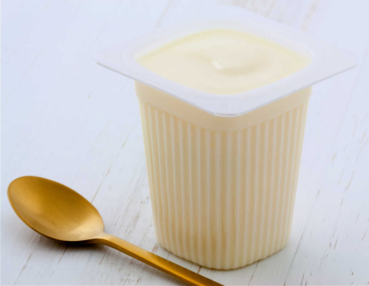 Plastic tub of plain yogurt next to a gold spoon.
