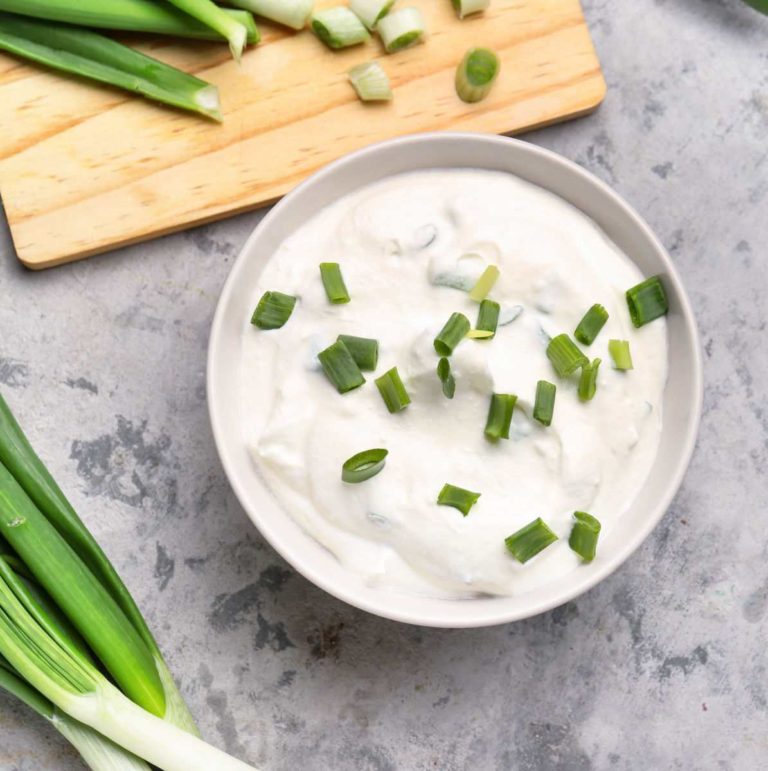 Bowl of sour cream with green onions and a cutting board.