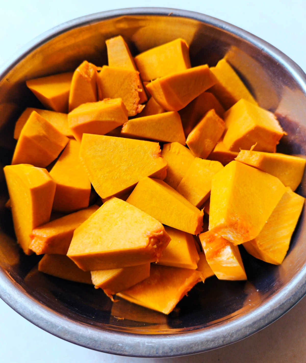 Cut the pumpkin into chunks A metal bowl holding pieces of cut up pumpkin.