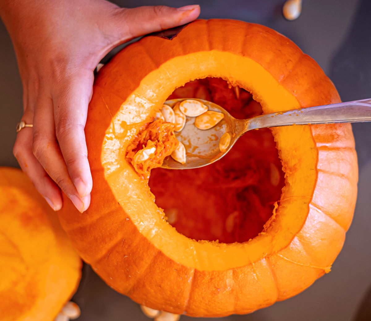 Remove the pumpkin seeds A woman holding a pumpkin and using a spoon to clean out the seeds from it.