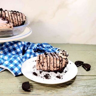 No-bake Oreo cheesecake recipe on a white plate near a cake stand and broken Oreo cookies.