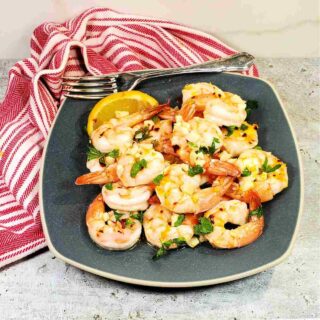 Shrimp on a gray plate with lemon and garlic near a striped red napkin.