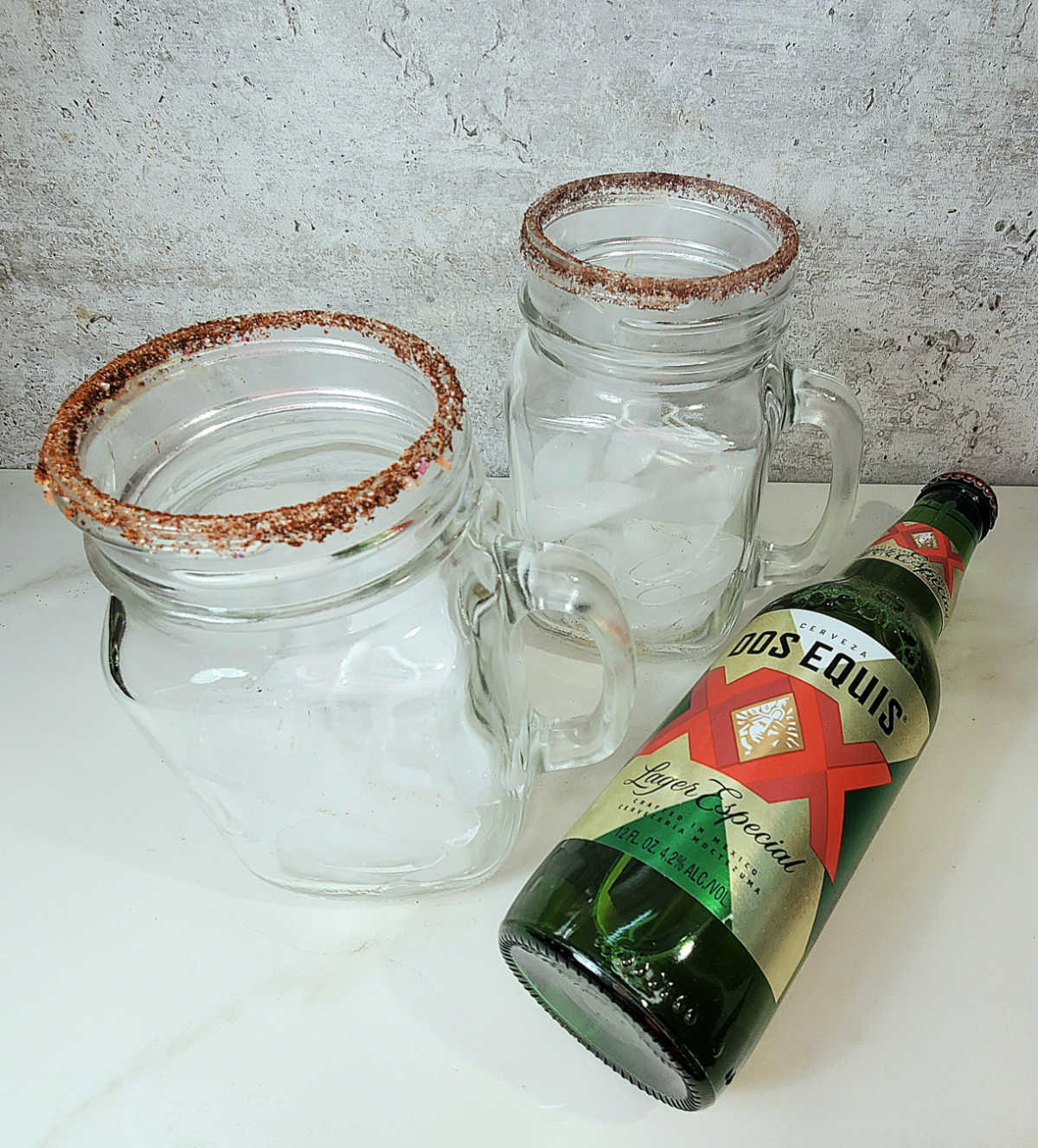 Two salt rimmed glasses next to a bottle of Mexican beer.