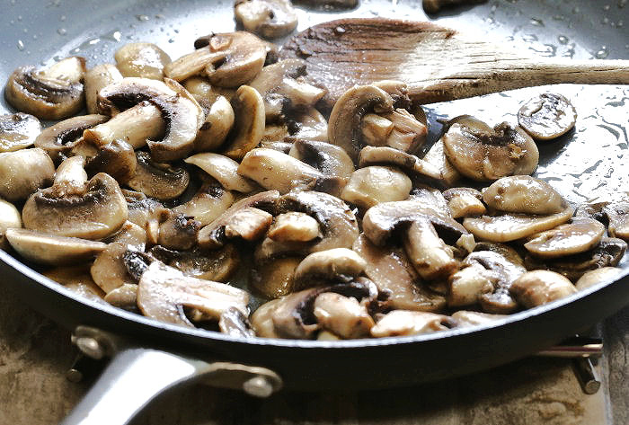Cooking sliced mushrooms in a pan for chicken scallopini.