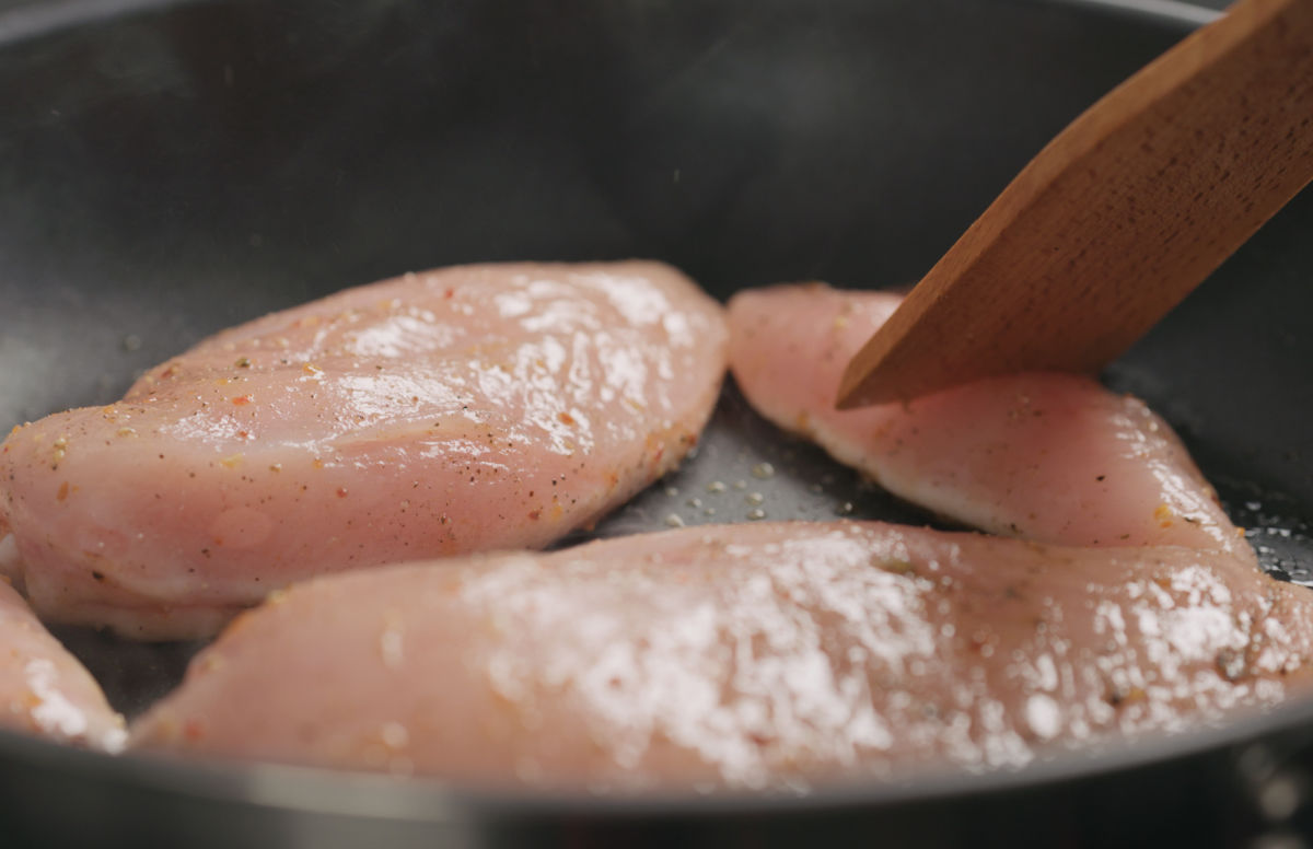 Cooking chicken breasts in a pan with a wooden spatula.