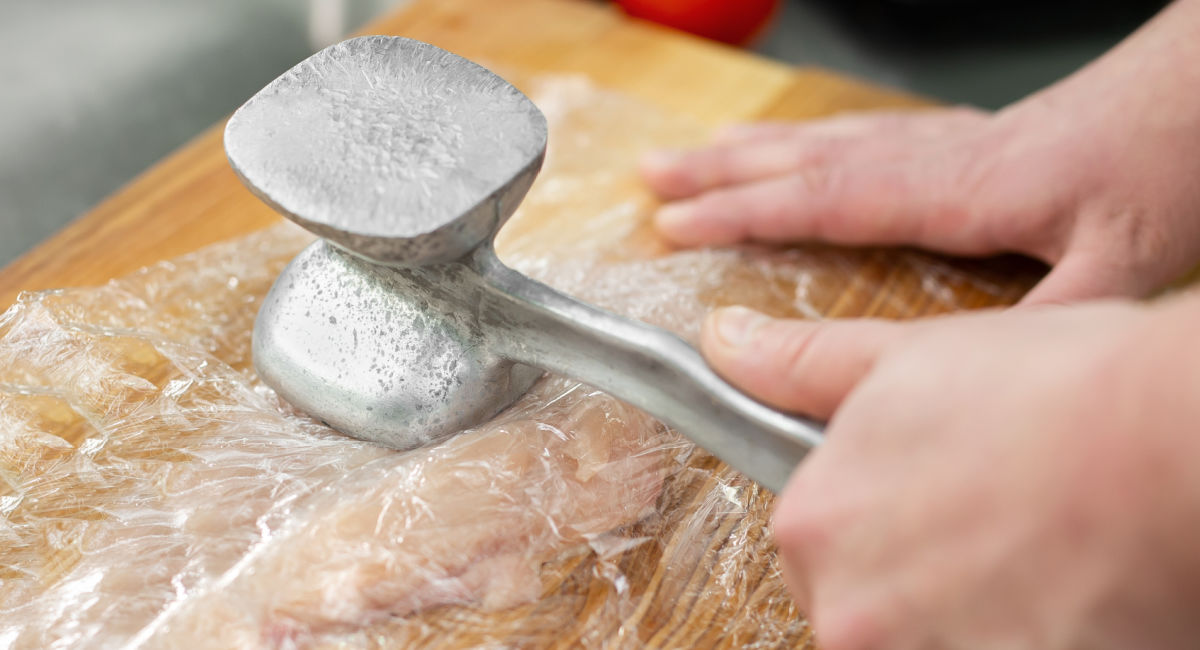 A woman with a meat tenderizer pounding chicken breasts.