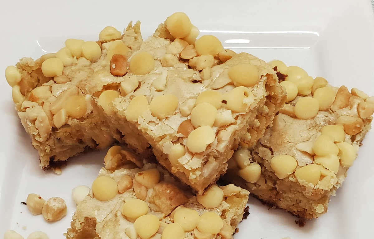 A close up of white chocolate and macadamia nut blondies on a white plate.