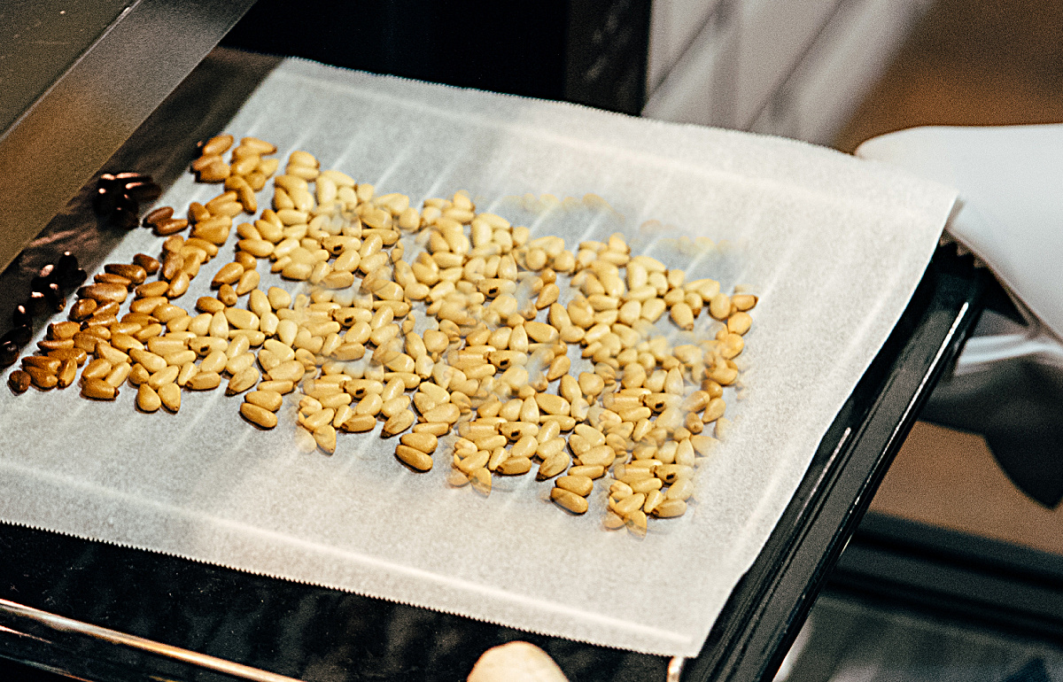 Hands holding a sheet pan with roasted pine nuts hot from the oven.
