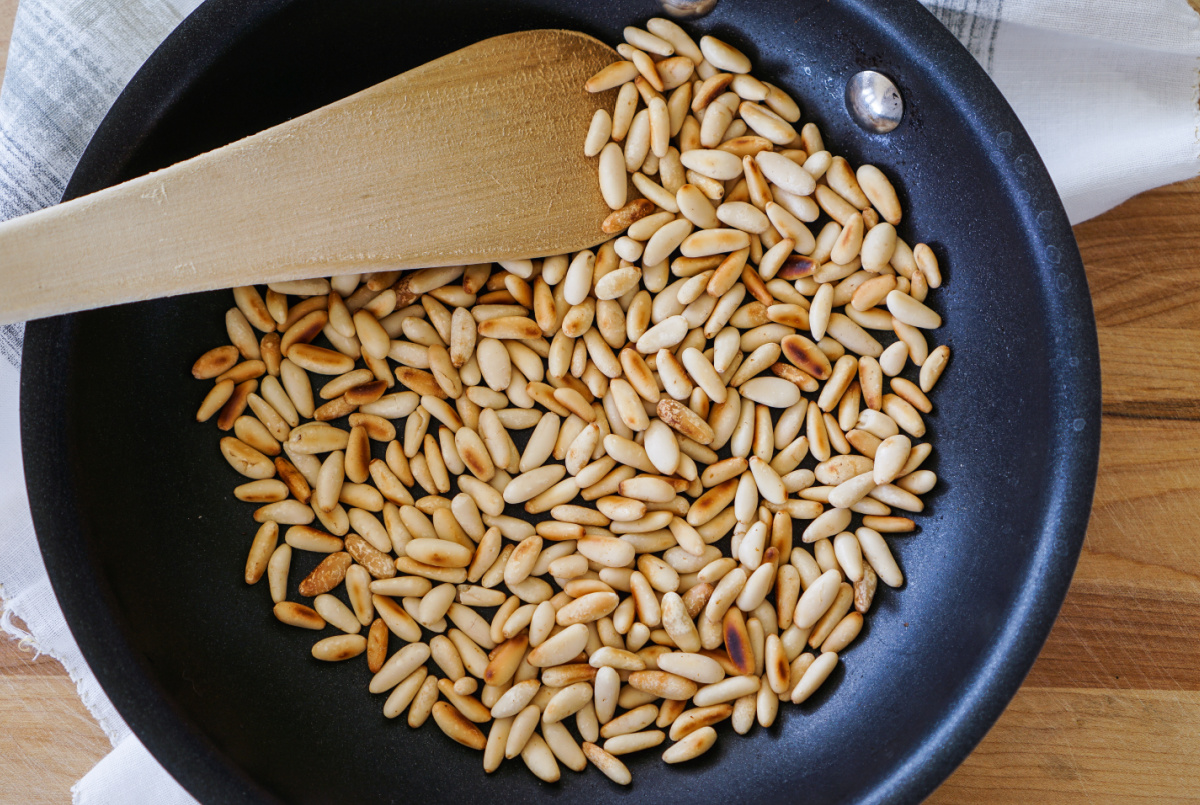 Toasted pine nuts in a dry frying pan with a spatula.
