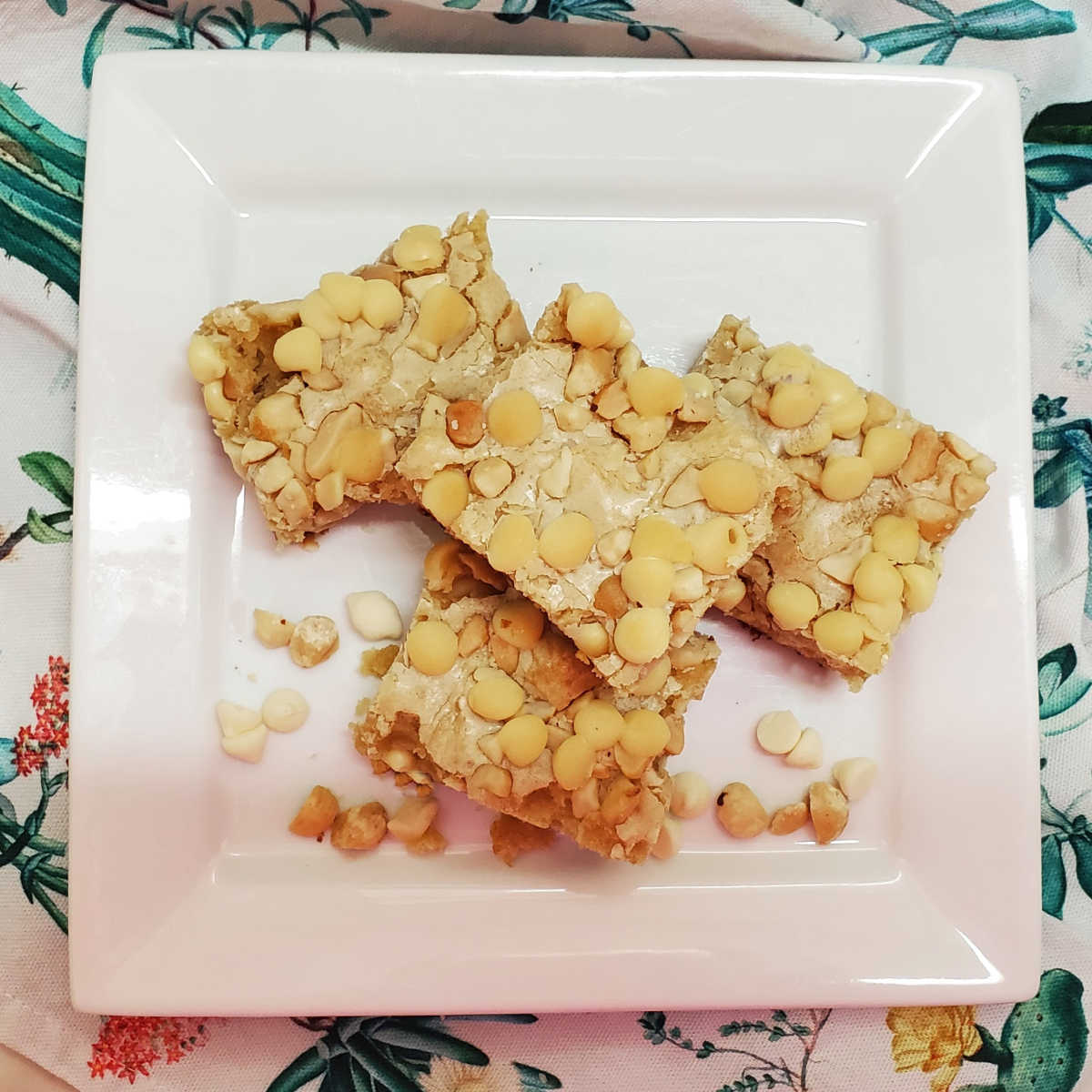 4 macadamia white chocolate bars stacked on a white plate over a colorful napkin.