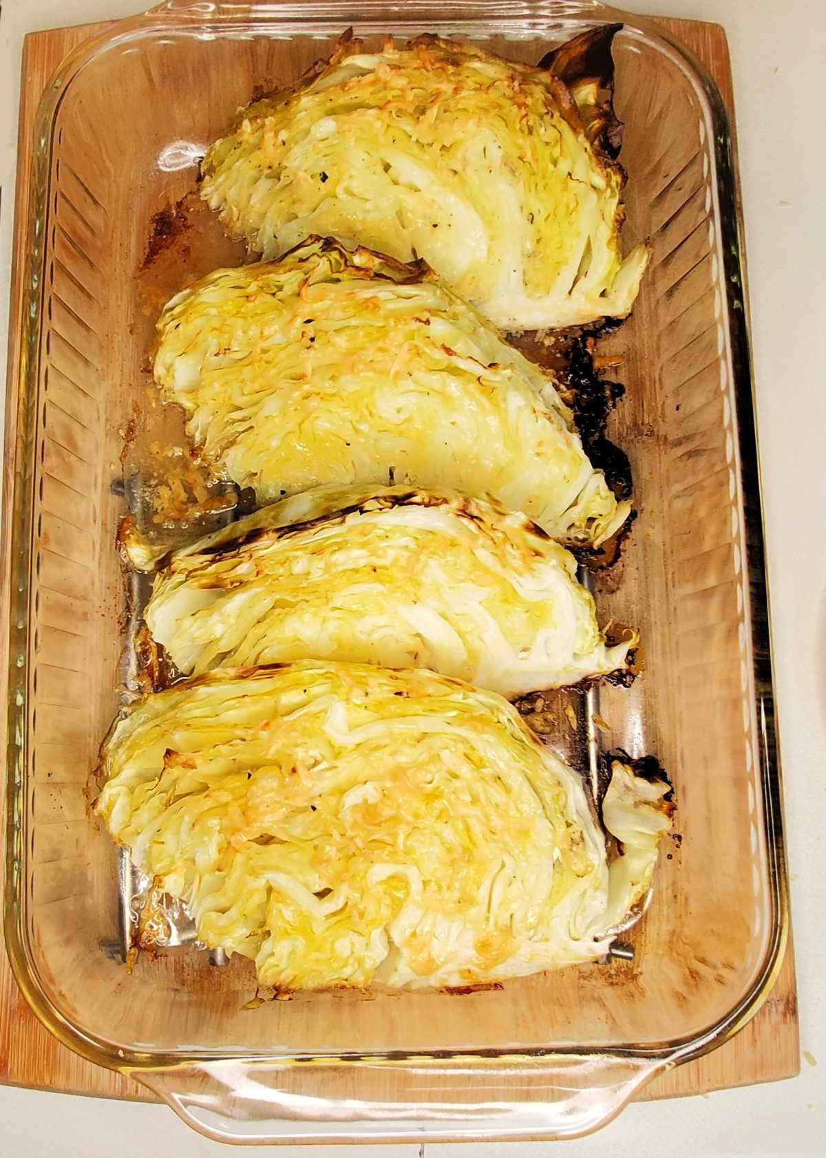 Roasted cabbage wedges in a glass baking dish on a cutting board.