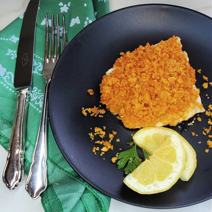 Crunchy baked cod recipe with Ritz cracker topping on a black plate with cutlery and a green napkin.