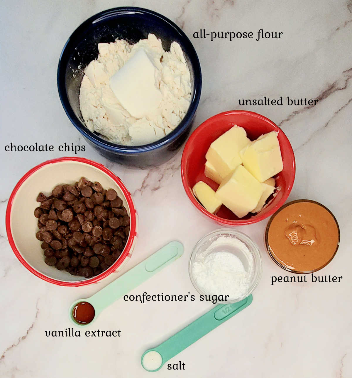 Ingredients for chocolate peanut butter shortbread cookies Bowls of flour, chocolate chips, butter, peanut butter, confectioner's sugar, salt and vanilla extract on a marble countertop.